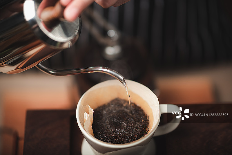 咖啡馆里的咖啡师把壶里的热水倒在咖啡粉上，来萃取刚煮好的咖啡。图片素材