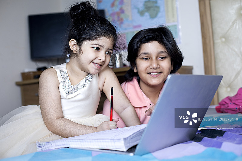 男孩在家里用笔记本电脑帮助小妹妹在线学习图片素材