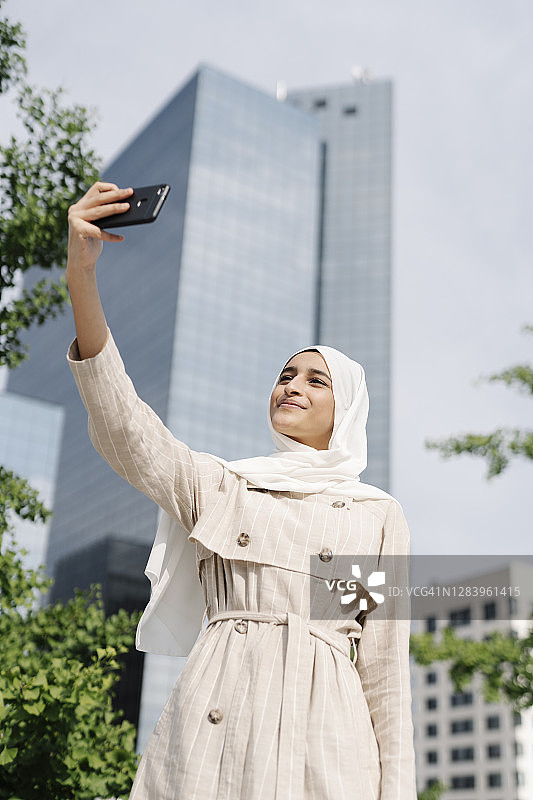 穆斯林少女在阳光明媚的日子里用智能手机自拍图片素材
