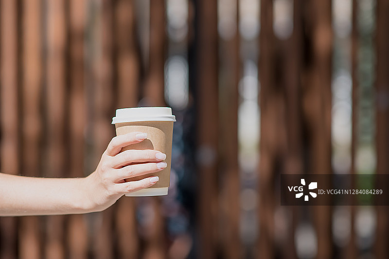 手拿一杯咖啡放在一个木制的背景上。咖啡日，咖啡爱好者们图片素材