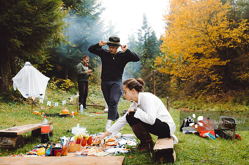 年轻的朋友们在森林里的篝火旁惬意地野餐图片素材
