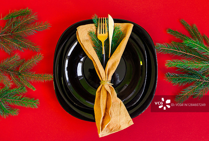 圣诞图片的盘子和餐巾与金色的刀叉在红色的背景，绿色的松树树枝。假日食物和餐桌的概念图片素材