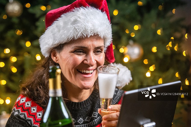 一个微笑的成熟女人用一杯香槟向她的家人敬酒，她正在使用电话会议图片素材