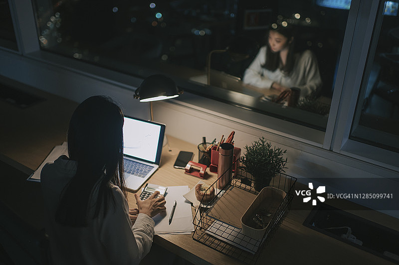 高角度亚洲华裔女性白领工作到深夜独自在办公室赶财务报告图片素材