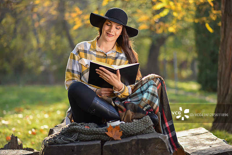 年轻漂亮的女人在秋天的阳光灿烂的一天在公园里看书图片素材
