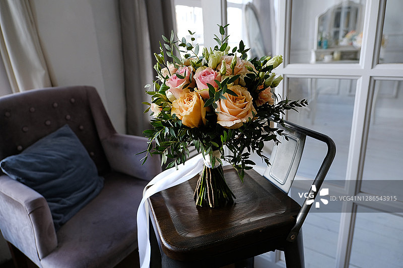 美丽的婚礼花束上原有的时尚木椅，特写。一束白色、米色、粉色的玫瑰和绿叶，用缎带系着，模糊了背景。婚礼的主题。图片素材