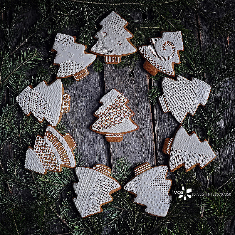 食物摄影，姜饼饼干在圣诞树的形式，手绘花边糖糖霜，周围的绿色云杉树枝在一个古老的木制纹理背景特写，俯视视图图片素材