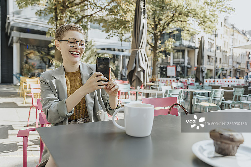 坐在户外咖啡馆里用智能手机自拍的女人图片素材