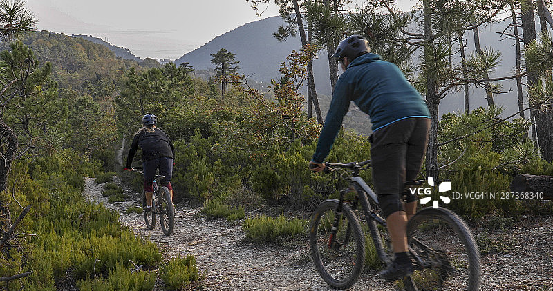山地自行车手在日出时沿着山坡上的小径骑行图片素材