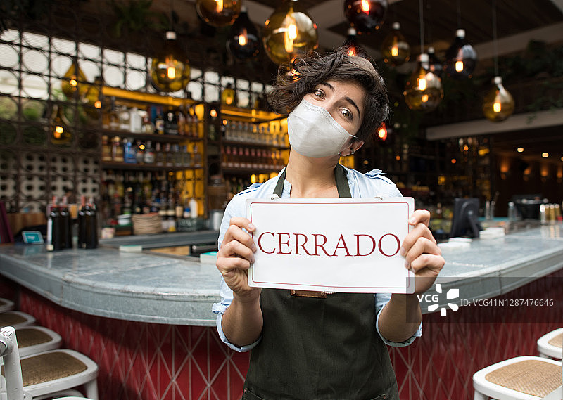 一名女子戴着面罩，举着西班牙语的餐馆关门标志图片素材
