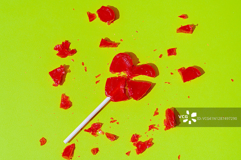 绿色背景上破碎的红色心形棒棒糖图片素材