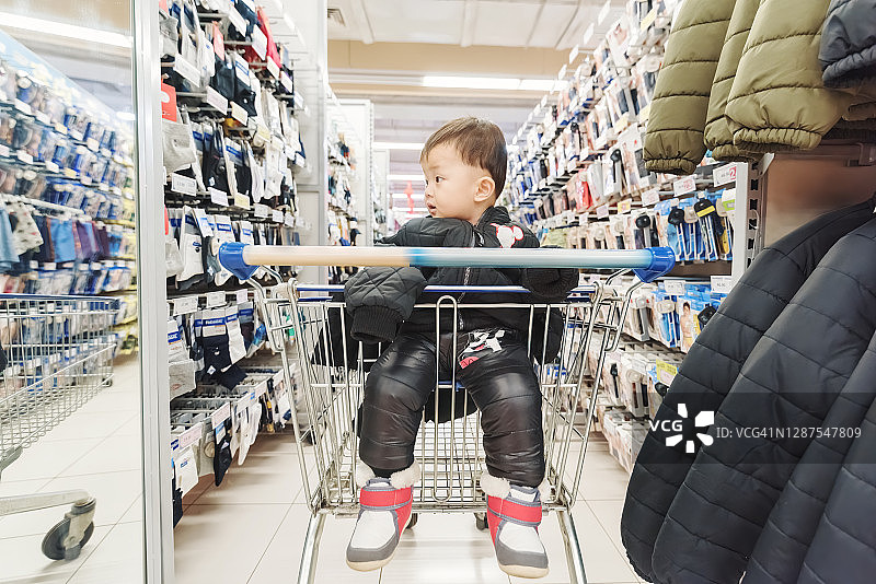 一个小男孩坐在超市的购物车里图片素材