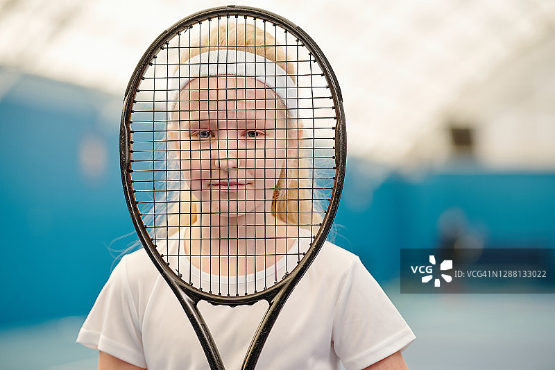 女孩穿着白色t恤，头带拿着网球拍在她面前图片素材