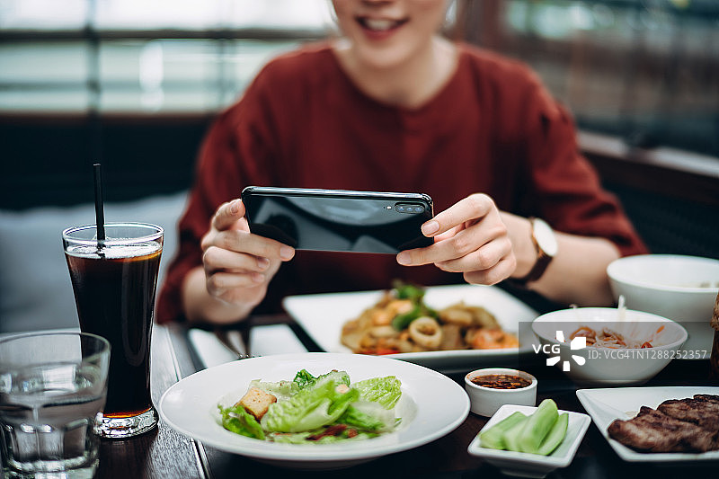 美丽微笑的年轻亚洲女子用智能手机拍下新鲜的泰国融合菜，并分享到社交媒体，然后去一家时尚的泰国餐厅吃图片素材