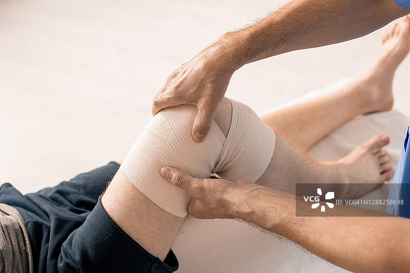 男性临床医师双手用弹性绷带包扎残疾患者膝关节图片素材