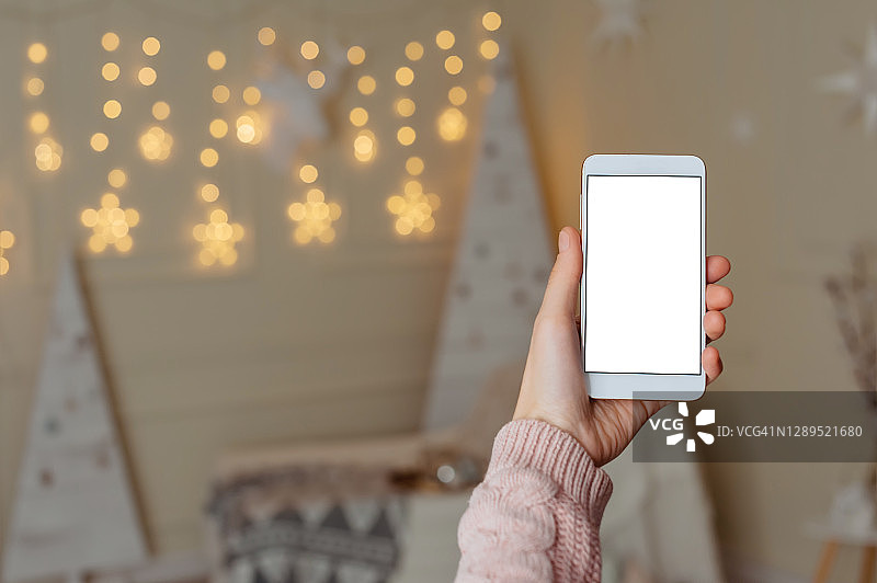 在圣诞装饰圣诞树的背景上，女孩手中的智能手机的模型。图片素材