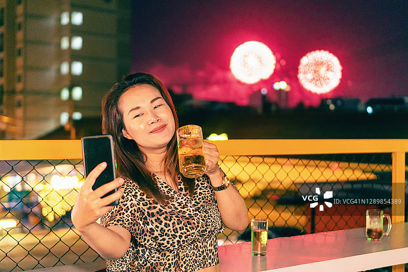 亚洲女人在烟花背景下喝着啤酒自拍图片素材