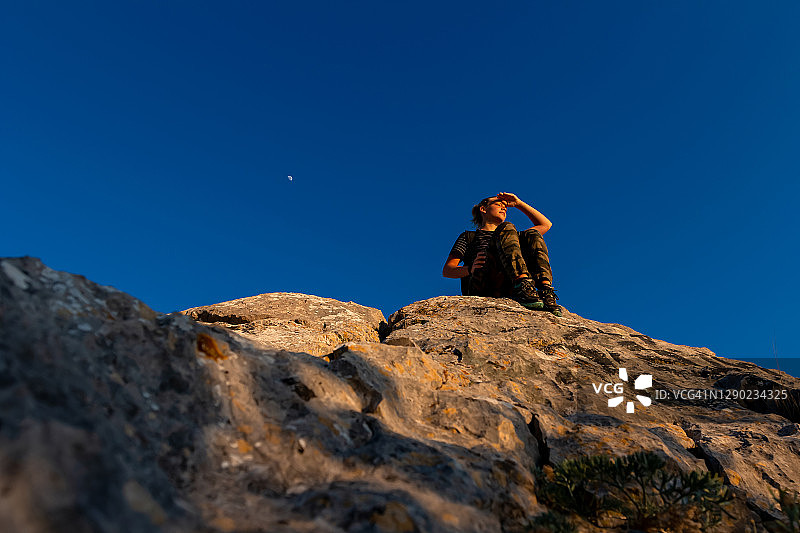 底部的观点，一个年轻的女孩旅行者坐在岩石上的背景与黑暗的天空与月亮图片素材