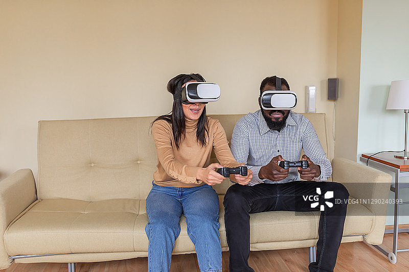 一个快乐的年轻女人正在客厅里用VR系统和她的男朋友玩电脑游戏。图片素材
