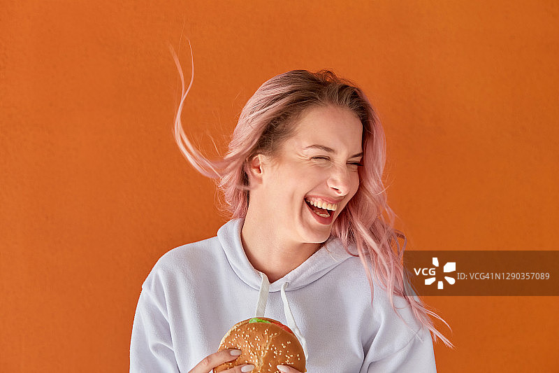 一个快乐的女人手里拿着一个大汉堡笑了。图片素材