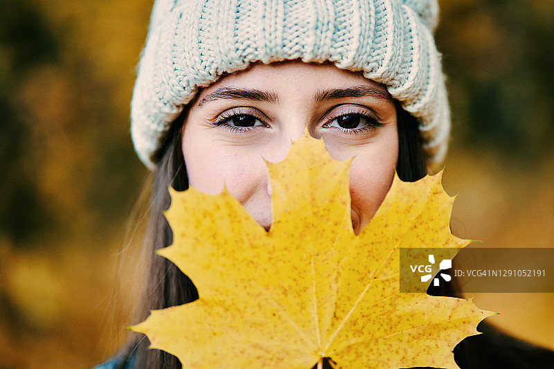 公园里，快乐美丽的年轻女子微笑着，用黄色的秋枫叶遮住了她的脸图片素材