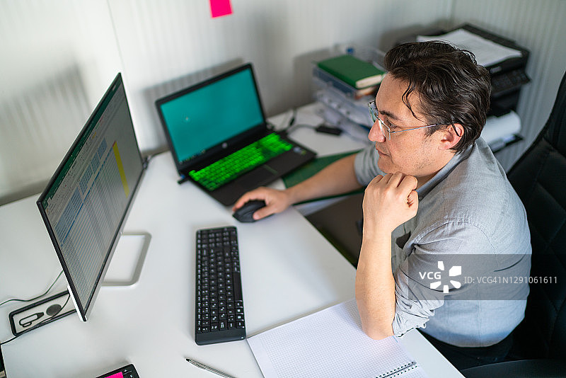 年轻的雇员坐在他的办公桌上检查他的电脑上的报告和图表图片素材