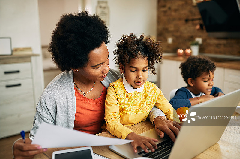 黑人工作母亲和她的女儿在家里使用笔记本电脑。图片素材