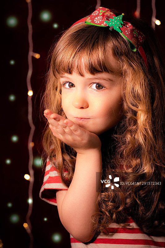 一个微笑的女孩在圣诞彩灯前飞吻的肖像图片素材