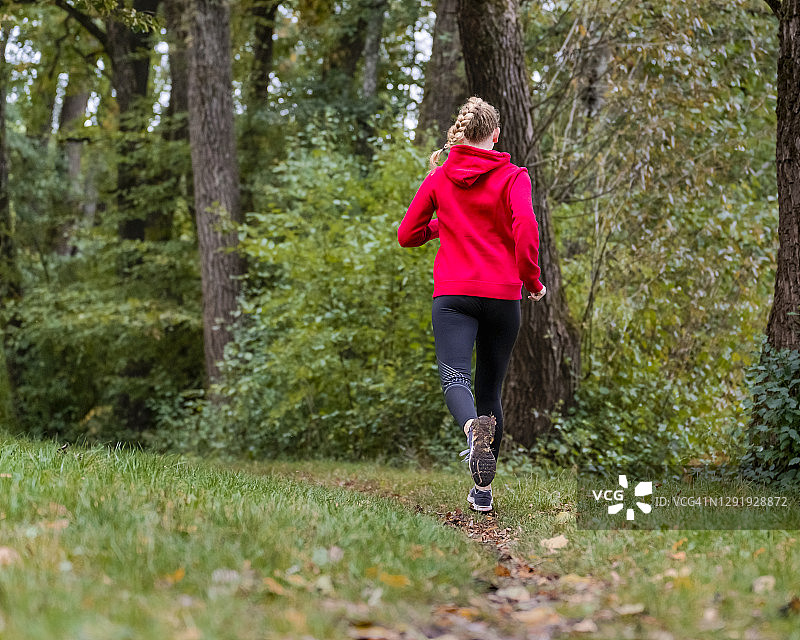 年轻的女运动员在森林的草地上慢跑图片素材