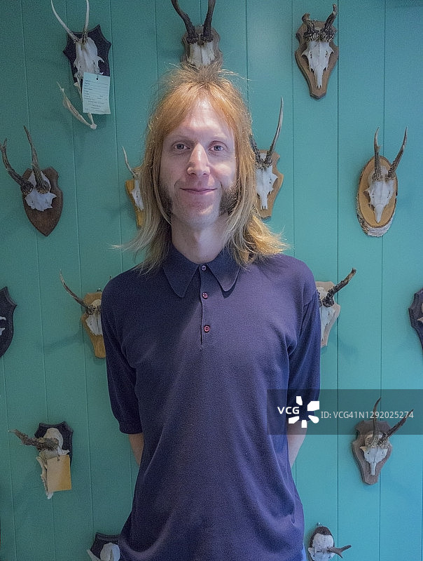 金发男理发师站在绿松石墙上动物头骨和鹿角图片素材