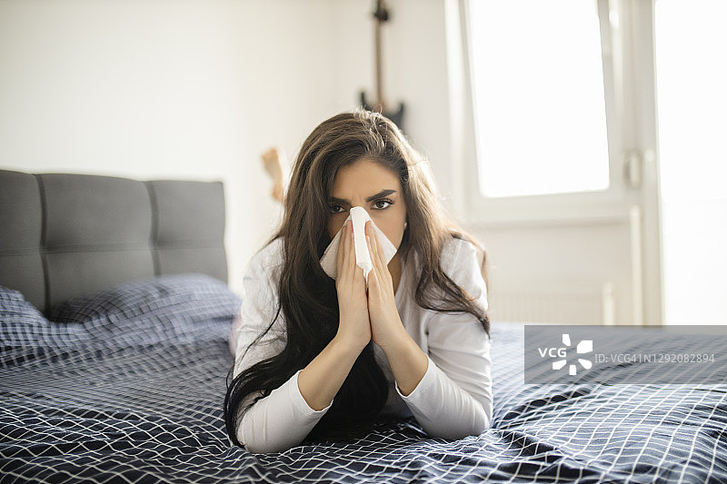 一个漂亮的年轻女子在家里躺在床上的时候患了流感图片素材
