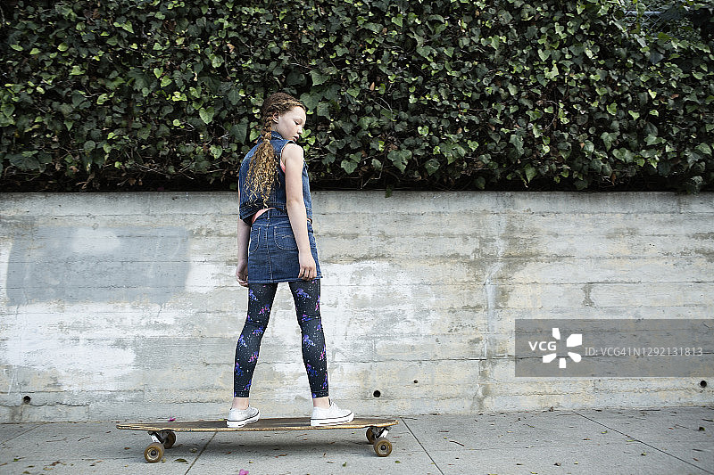 女孩滑板在人行道上的后视图图片素材