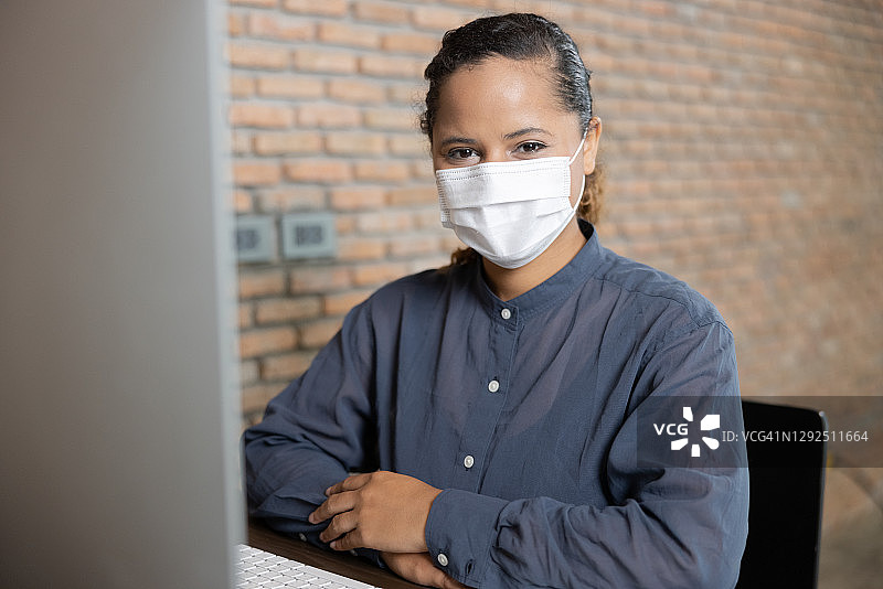 混血，非裔美国妇女，戴着防护面具在电脑上工作图片素材