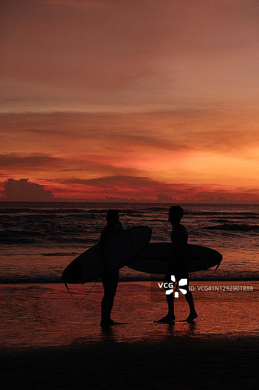 日落时，冲浪者的剪影走过海岸图片素材