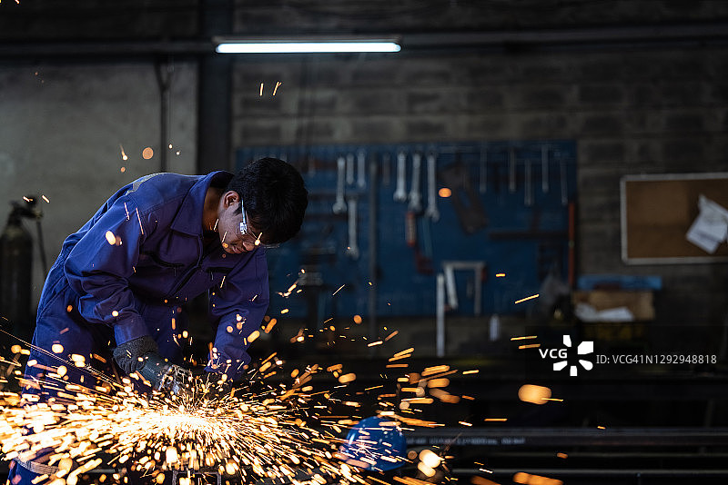 男工人戴着安全眼镜和蓝色工作服，在工厂车间焊接金属，火花飞溅图片素材