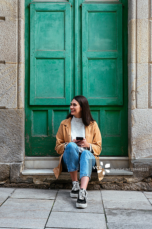 年轻时尚的女人坐在户外用着智能手机图片素材