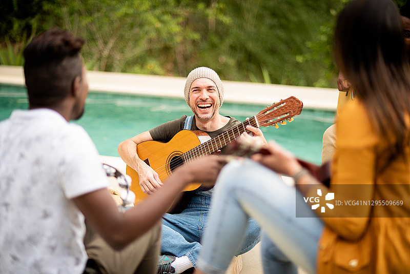 一个年轻人和一群不同的朋友在外面弹吉他图片素材
