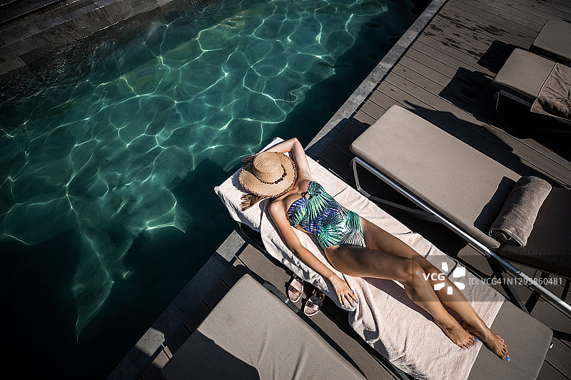 一个女人在游泳池旁的躺椅上休息图片素材