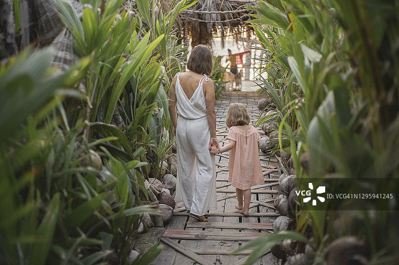 母亲和女儿手牵着手走在热带度假胜地的木板路上图片素材
