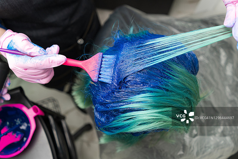 在染发过程中，发型师戴着防护手套，用粉红色的毛刷给顾客涂上蓝色的油漆图片素材