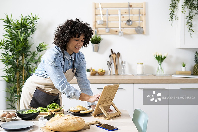 一名年轻女子在厨房用平板电脑准备素食三明治图片素材