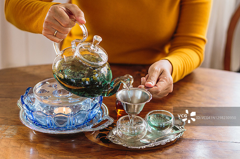 女子将茶从玻璃壶倒入杯中，茶道概念图片素材