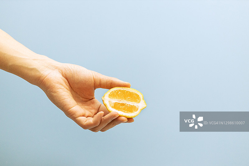 手拿新鲜的橙子在蓝色的背景图片素材