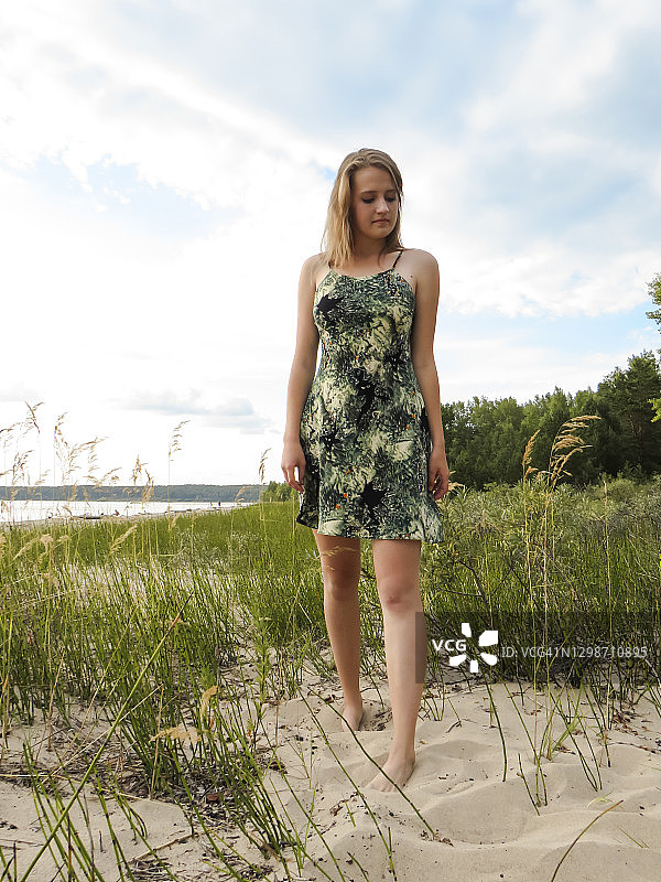 美丽的年轻的金发女人在一个炎热的夏天在一个沙滩上的一个短的夏天的海滩上以绿色的森林和多云的天空为背景图片素材