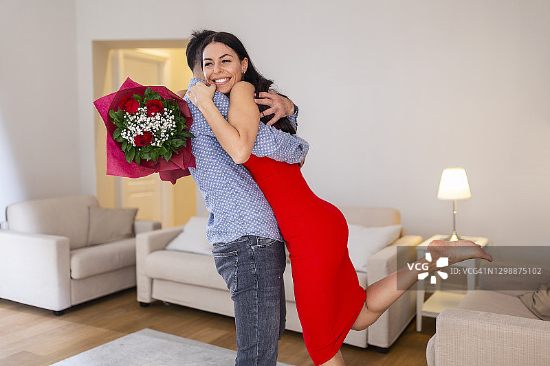 漂亮的年轻夫妇在家。拥抱，亲吻，享受在一起的时间，用红玫瑰庆祝情人节图片素材