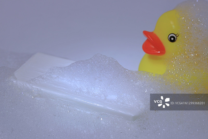 白色的肥皂带肥皂泡沫和一个黄色的橡胶鸭子在白色的背景图片素材