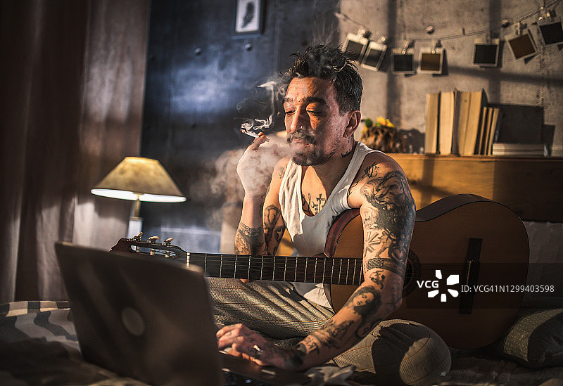 有纹身的嬉皮士坐在床上弹原声吉他，图片素材