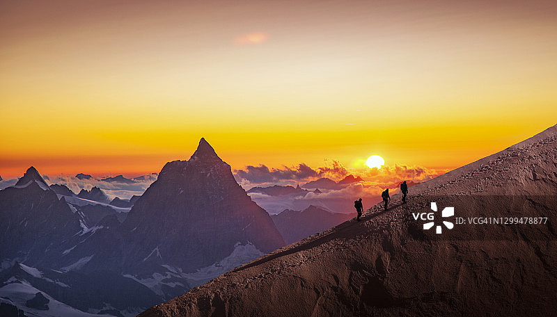 日出时攀登者站在积雪的山脊上图片素材