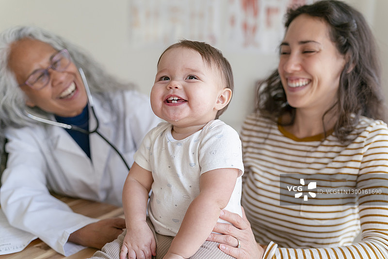 高级女医生正在为微笑的婴儿病人和她的母亲做健康检查图片素材
