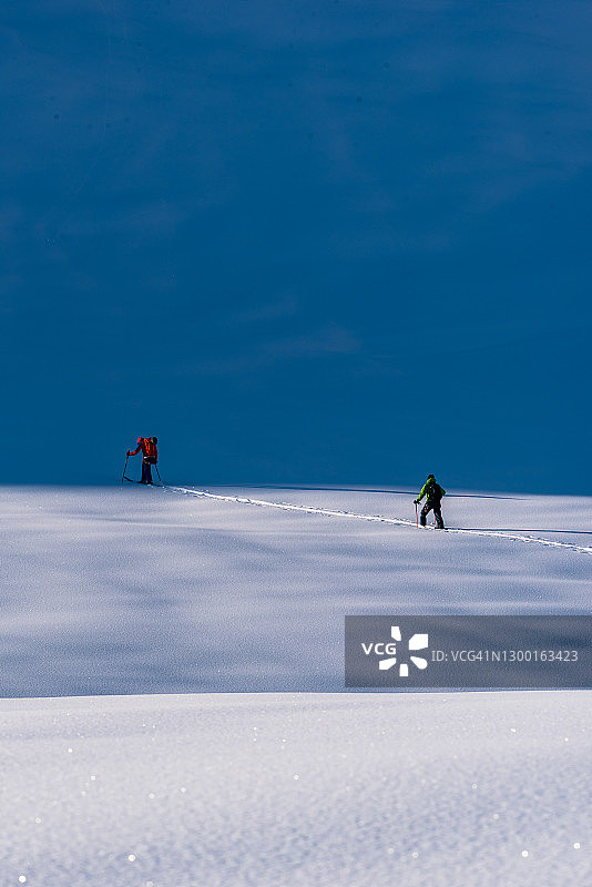 滑雪登山运动员攀登高耸的山脉下的雪坡图片素材